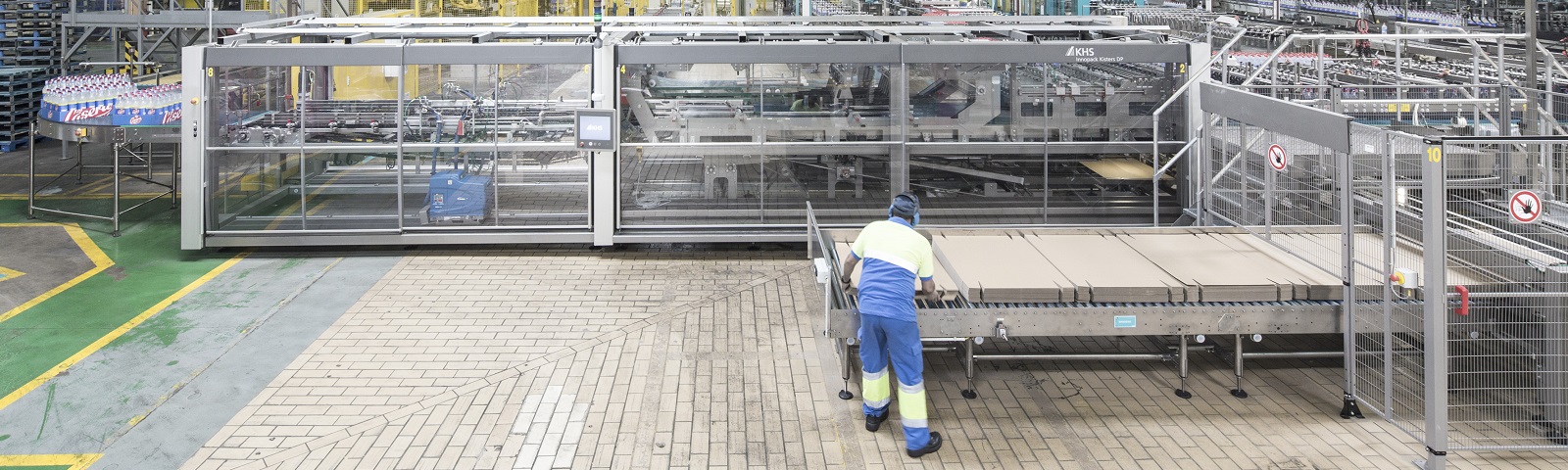 Ein Arbeiter in einer Produktionshalle bedient eine große Verpackungsmaschine, um Kartons zu transportieren.