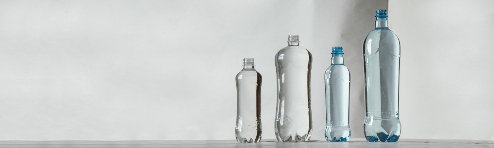 Das Bild zeigt vier PET-Flaschen in verschiedenen Größen und Designs, die nebeneinander vor einem schlichten Hintergrund aufgestellt sind und modernes Behälterdesign repräsentieren.